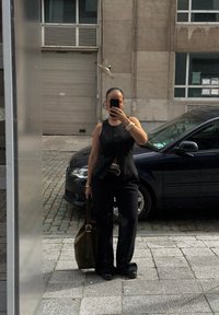 Μαύρο αμάνικο τοπ με κουμπιά, ψηλόμεσα μαύρα παντελόνια και μια σκούρα τσάντα tote. Υφασμάτινη επιφάνεια με λαμπερά αξεσουάρ κοσμημάτων.