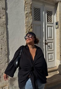 Chemise noire texturée à manches longues avec un nœud à l'avant. Jean bleu clair et petit sac à main noir. Accessoires unis.