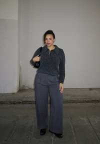 Grijze gebreide trui met een kraag en donkergrijze broek met brede pijpen, gecombineerd met zwarte schoenen en een kleine zwarte handtas. Geen opvallende patronen.