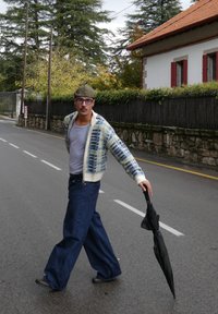 Mees kõnnib tänaval, kandes mustrilist, kootud rohelise-ja sinise kardigaani, halli t-särki, lahtisi siniseid teksapükse ning hoides musta vihmavarju.