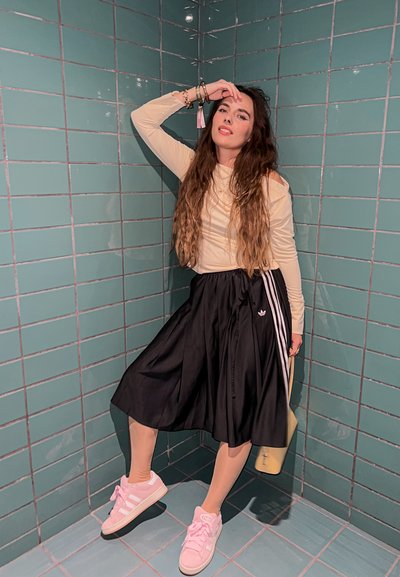 Top de manga larga de color beige claro combinado con una falda negra hasta la rodilla con rayas blancas. Zapatillas rosas y accesorios completan el conjunto.