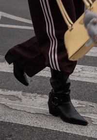 Botines de cuero negro con punta afilada y tacón grueso, con una correa ancha y detalle de hebilla.