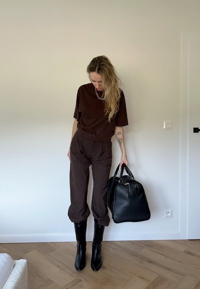 Camiseta oversized marrón, pantalones marrones a juego, botas negras hasta el tobillo y un bolso de cuero negro. Texturas suaves; diseño minimalista.