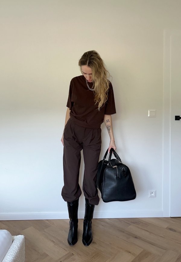 Hnědé oversized tričko, odpovídající hnědé kalhoty, černé kotníkové boty a černá kožená taška. Hladké textury; minimalistic design.