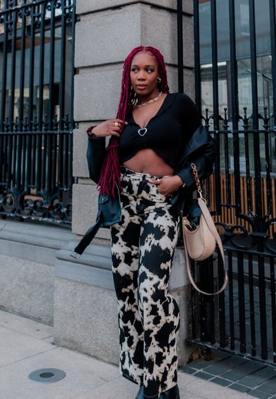 Top recortado negro con acento en forma de corazón, combinado con jeans de pierna ancha de cintura alta en blanco y negro con patrón. Chaqueta de cuero y bolso.