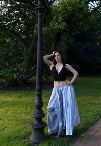 Črn skrajšan top z globokim V-izrezom, v kombinaciji z velikanskimi svetlo modrimi širokimi hlačami. Model pozira ob okrasnem uličnem svetilniku v zelenju.