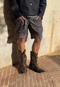 Pruun nahast cowboy-saapad, millel on tikandi detailid, koos hallide lühkaritega ja tumeda denimpikaga. Lilleline riietus erinevate tekstuuridega.