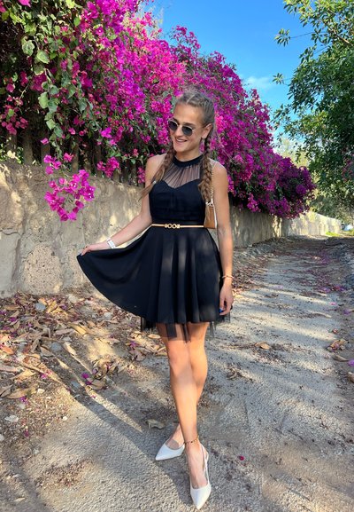 Vestido negro con un corsé ajustado, superposici&oacute;n transparente y falda plisada. Combinado con tacones blancos de punta y un cintur&oacute;n dorado.