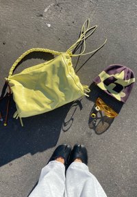 Chaussures noires sur un trottoir gris près d'un sac à main jaune, d'un bonnet violet et jaune, de lunettes de soleil jaunes et de trois bagues disposées au soleil.