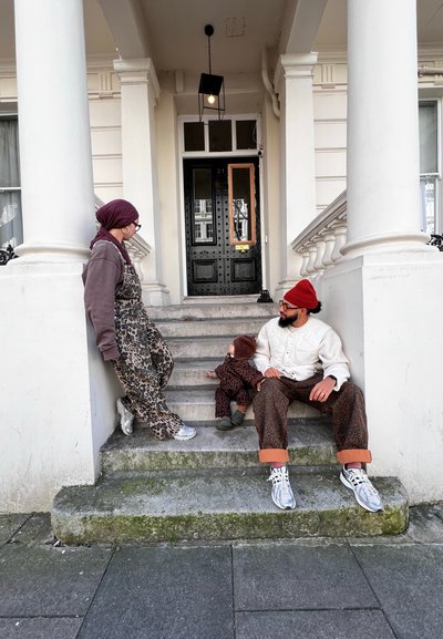Ropa con estampado de leopardo en tonos marrones, una chaqueta acolchada ligera y gorros de punto. Escaleras de piedra conducen a una puerta principal negra con herrajes intrincados.