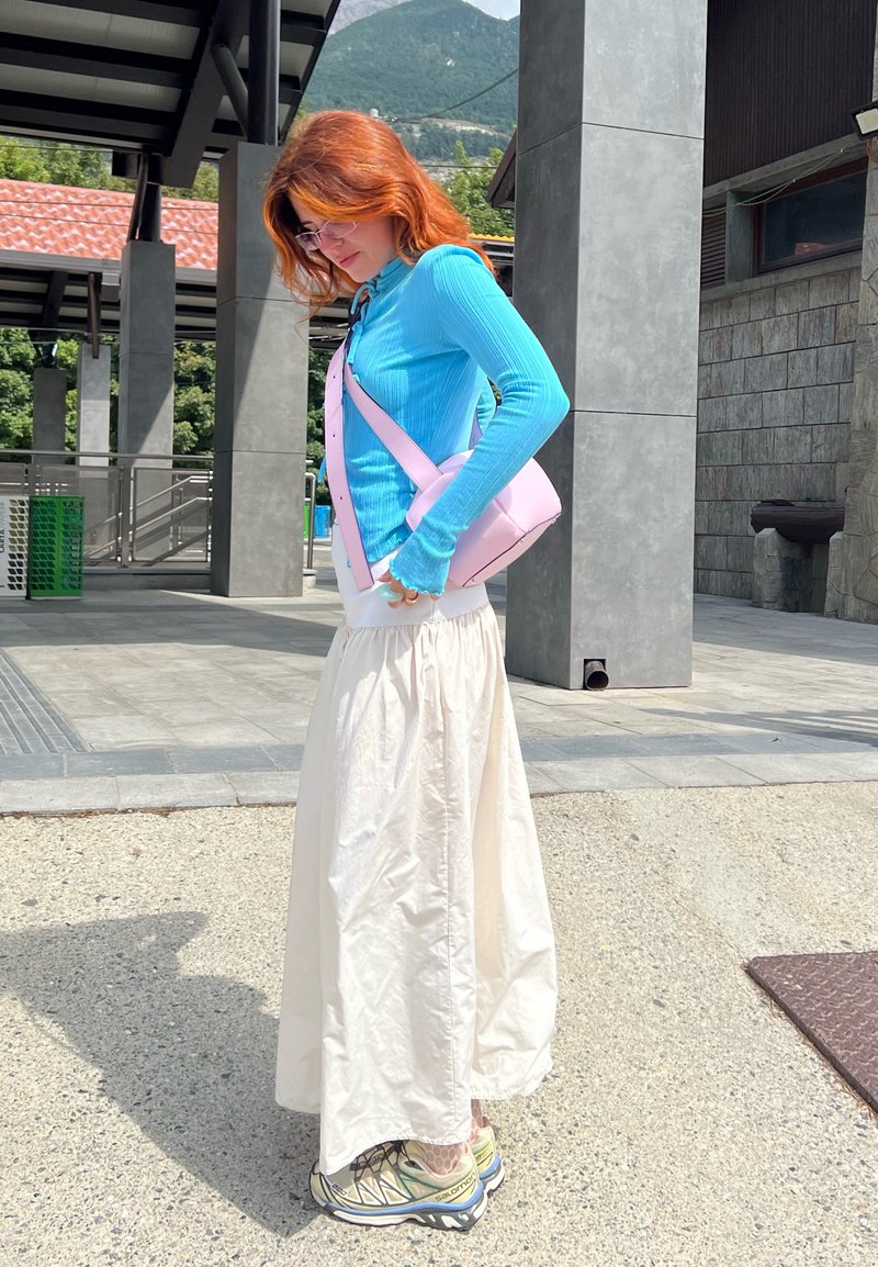 Ανοιχτό μπλε ριγέ κολλητό πουκάμισο με μακριά μανίκια, εκρού maxi φούστα, ροζ τσάντα χιαστί και μπεζ παπούτσια πεζοπορίας, σε φόντο μοντέρνου κτηρίου.