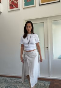 Witte aansluitende crop top, crèmekleurige wikkelrok met strikdetail, natuurlijke stoftextuur en minimaal ontwerp. Neutrale tinten tegen een lichte achtergrond.