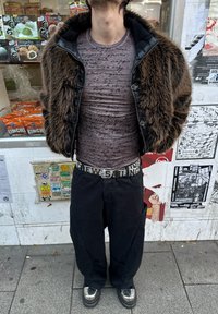 Brown faux fur jacket with a black collar, patterned grey shirt, black trousers, and silver platform shoes. The belt reads "CREW SAILING."