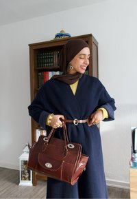 Manteau cache-cœur bleu marine avec une ceinture à la taille, top jaune en dessous, et sac à main en cuir marron avec ferrures argentées et détail d'une poche avant.