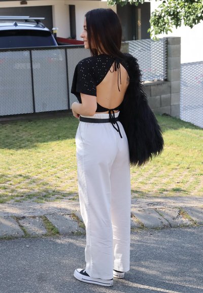 Top negro de espalda descubierta con mangas cortas, combinado con pantalones blancos de pierna ancha y zapatillas negras. Presenta una tela texturizada y un diseño atado en la parte posterior.
