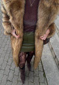 Manteau en fausse fourrure marron, haut bordeaux scintillant, mini-jupe en cuir verte, collants résille noirs et bottes marron montantes. Accessoires : un collier et une bague.
