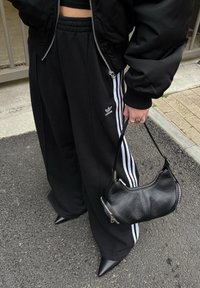 Μαύρο bomber μπουφάν με ριχτές μανσέτες, σε συνδυασμό με φαρδιά μαύρα παντελόνια φόρμας με λευκές ρίγες στα πλάγια. Μαύρη δερμάτινη τσάντα με φερμουάρ.