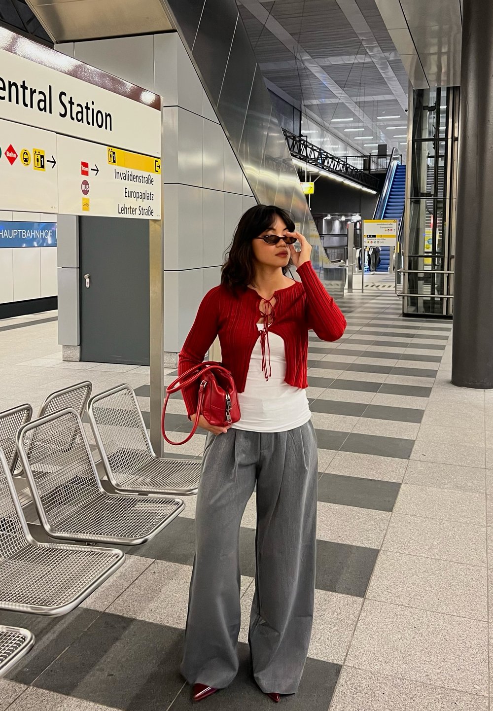 Rød ribbet kort cardigan over en hvid bluse, grå brede bukser og røde spidse hæle. Accessories inkluderer en lille rød taske og solbriller.