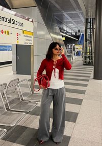 Rød ribbet kort cardigan over en hvid bluse, grå brede bukser og røde spidse hæle. Accessories inkluderer en lille rød taske og solbriller.