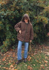 Barna steppelt dzseki zöld díszítéssel, világos pulóver és kék farmer felett viselve. Barna bokacsizmák és egy zöld táska egészítik ki a megjelenést.