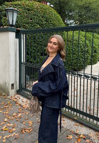 Chaqueta de mezclilla oscura con mangas oversize y cintura ceñida, combinada con pantalones de mezclilla oscura a juego. Sosteniendo un bolso marrón claro.