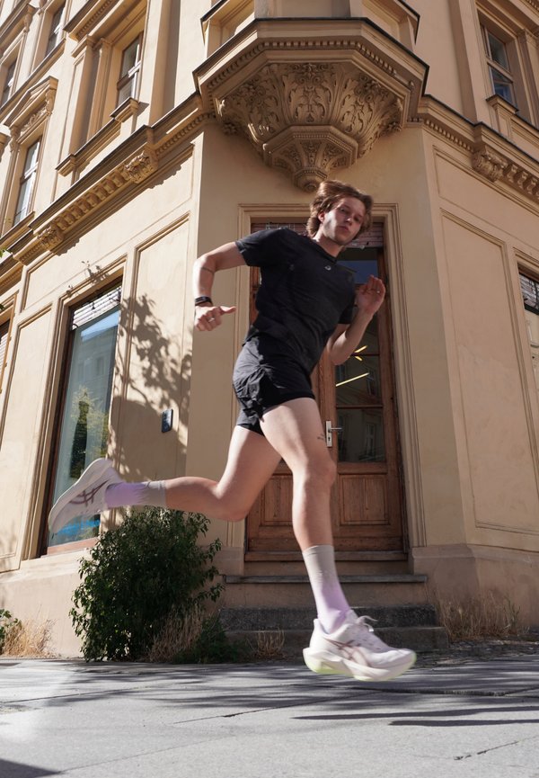 Jeune homme en tenue de sport noire courant devant un bâtiment historique beige avec une porte en bois et des détails architecturaux décoratifs.
