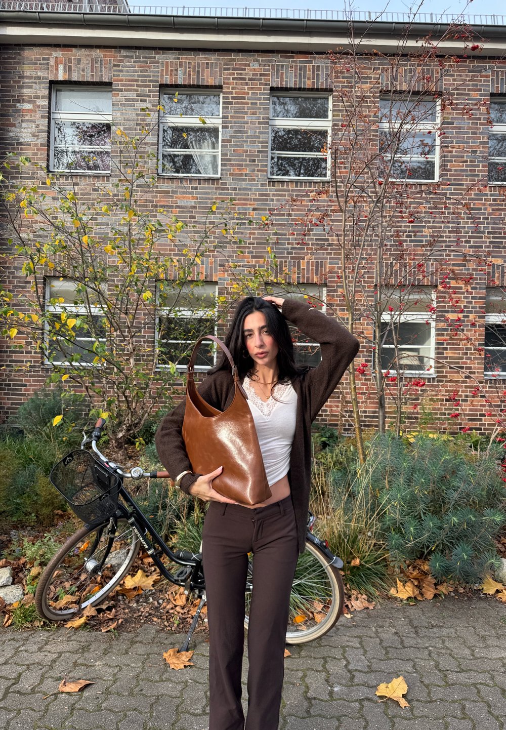 Brown leather tote bag with a smooth finish, wider at the top and tapering down. Features a single shoulder strap and minimalist design.