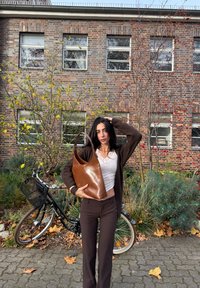 Brown leather tote bag with a smooth finish, wider at the top and tapering down. Features a single shoulder strap and minimalist design.