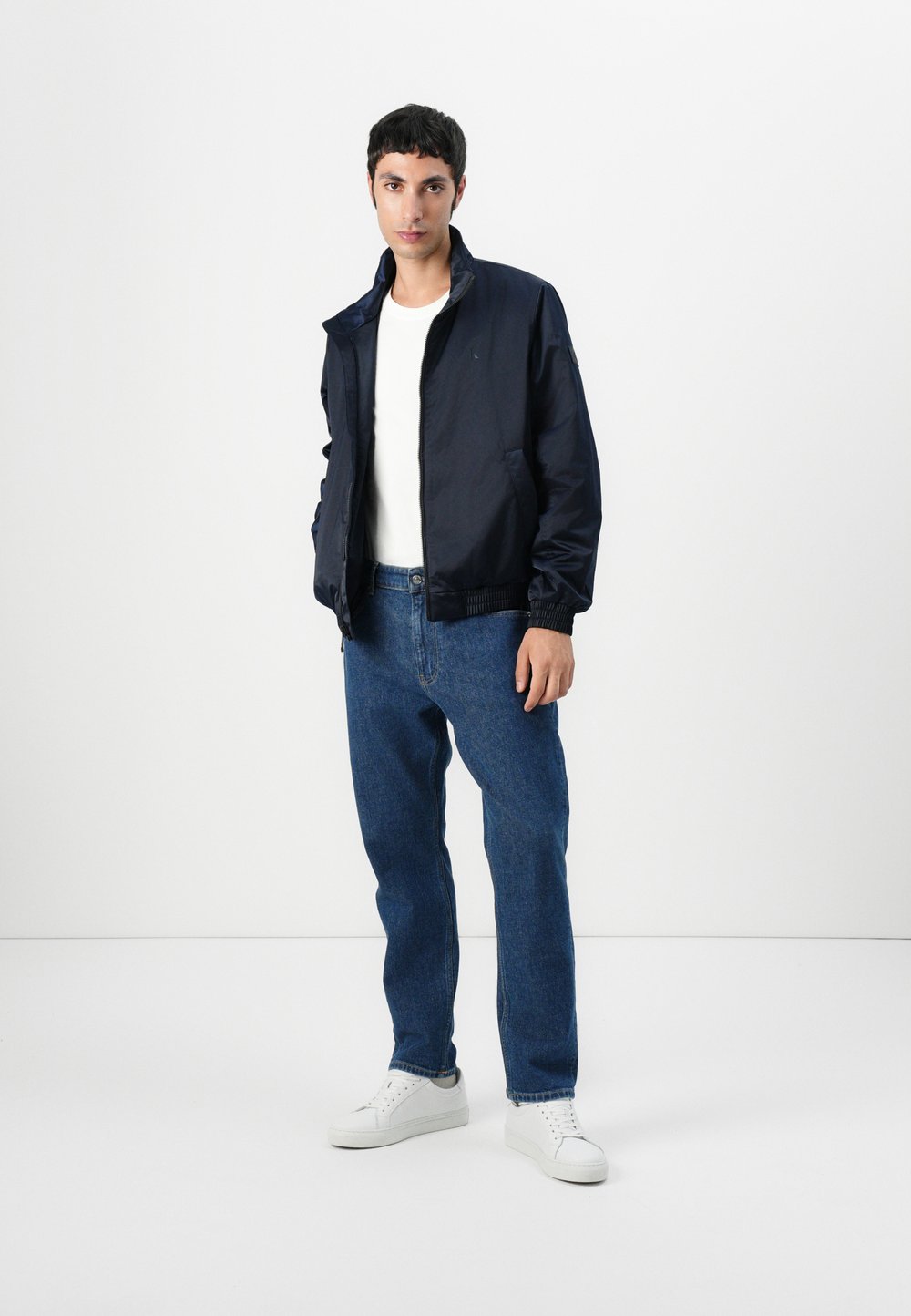 Tengeri bomber dzseki felálló gallérral, kék farmernadrággal és fehér tornacipővel párosítva. Sima anyag, rugalmas mandzsettákkal és derékpánttal.