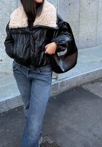 Veste en cuir noir avec un col en fausse fourrure crème, associée à un jean bleu à jambes droites. Comprend un grand sac à main noir et des matériaux texturés.