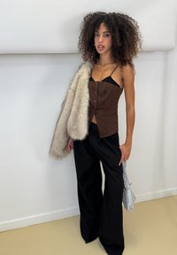 Chaleco marrón ajustado con botones, tirantes negros transparentes, pantalones anchos negros y un chal de piel sintética. Accesorios con un bolso plateado brillante.