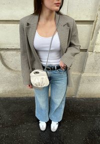 Rutigt blazer i beige och brunt, vit linne, ljusblå vida jeans, krämfärgad handväska med strukturerad finish och vita sneakers.