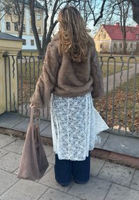 Hnědá umělá kožešinová bunda, bíl dress s krajkovým přesahem, široké modré džíny a béžová taška. Dlouhé vlnité vlasy viditelné zezadu.