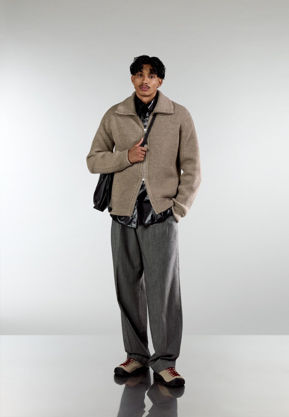 Beige ribbed knit jumper with a zip fastening, layered over a black shirt, paired with grey wide-leg trousers and multicoloured shoes.
