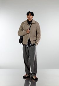 Beige ribbed knit jumper with a zip fastening, layered over a black shirt, paired with grey wide-leg trousers and multicoloured shoes.