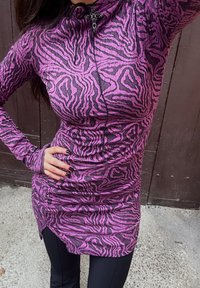 Haut ajusté à manches longues avec imprimé zèbre rose et noir, doté d'un col haut et d'un pendentif croix décoratif noir. Tissu texturé avec un aspect superposé.