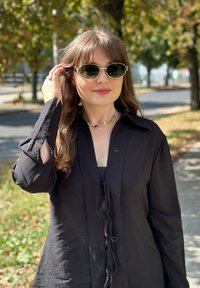 Μαύρο μπλουζάκι με μακριά μανίκια και λεπτομέρεια κόμπου μπροστά, σε συνδυασμό με στρογγυλά γυαλιά ηλίου και πολύχρωμο περιδέραιο από χάντρες σε εξωτερικό χώρο.