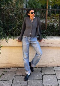 Γκρι ζακέτα με κουμπιά, λευκό πουκάμισο, χαλαρά ανοιχτό μπλε τζιν και μαύρες loafers. Είναι ορατά επίσης γυαλιά ηλίου και μια μαύρη τσάντα.