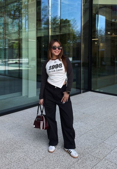 Camisa de manga larga blanca y negra con texto, pantalones anchos negros, zapatillas blancas con rayas negras y un pequeño bolso burdeos.