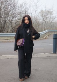 Sorte vide bukser kombinert med en svart topp og skjerf. En lilla og brun teksturert håndveske med pigger, båret over kroppen.