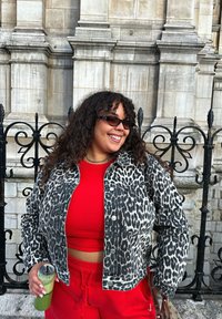Leopard print denim jacket over a red ribbed crop top, paired with red sweatpants. Holding a green drink in a clear cup. Black sunglasses.