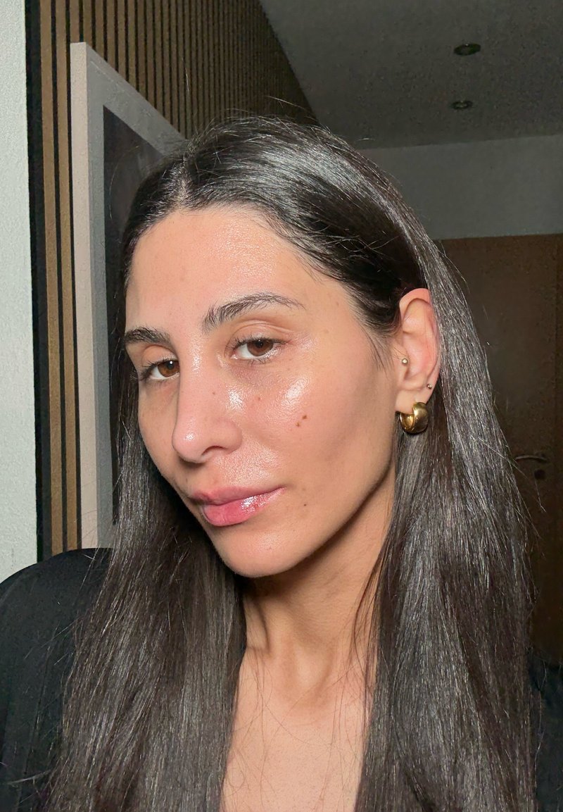 Primo piano ritratto con capelli lisci e scuri; indossa grandi orecchini a cerchio dorati. La pelle è liscia con una leggera lucentezza; tratti del viso sottili e visibili.