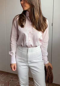Světle růžová košile na knoflíky vyrobená z měkké tkaniny; spárována s bílými kalhotami s vysokým pasem. Doplňky zahrnují hnědou texturovanou kabelku.