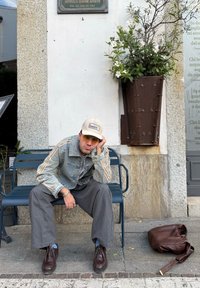 Jeans jakna z črtastimi rokavi, sivi široki hlače, rjavi čevlji z vezalkami in bež kapa. Rjava usnjena torba leži na tleh.