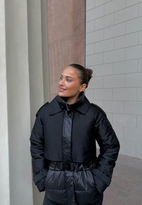 Czarna kurtka puchowa o krótkim kroju, z dużym kołnierzem i paskiem w talii. Charakteryzuje się błyszczącą fakturą i przednimi kieszeniami.