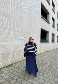 Μαύρο και άσπρο ριγωτό πουλόβερ με υπερμεγέθη μανίκια, συνδυασμένο με μακριά ναυτικό φούστα και μαύρες μπότες μέχρι τον αστράγαλο. Το φόντο περιλαμβάνει μια υφασμάτινη τοιχοποιία.