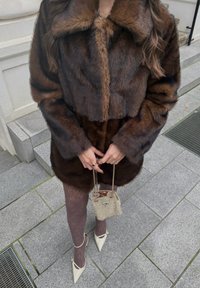 Rudos spalvos dirbtinio kailio trumpas paltas su plačia apykakle, derinamas su tamsiomis pėdkelnėmis nėriniuotu raštu ir baltais smailiais aukštakulniais. Maža metalinė rankinė.