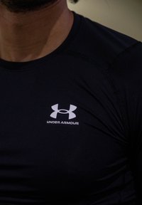 Black sports shirt with short sleeves, made of smooth fabric. Features a white Under Armour logo on the chest and visible seam detailing.