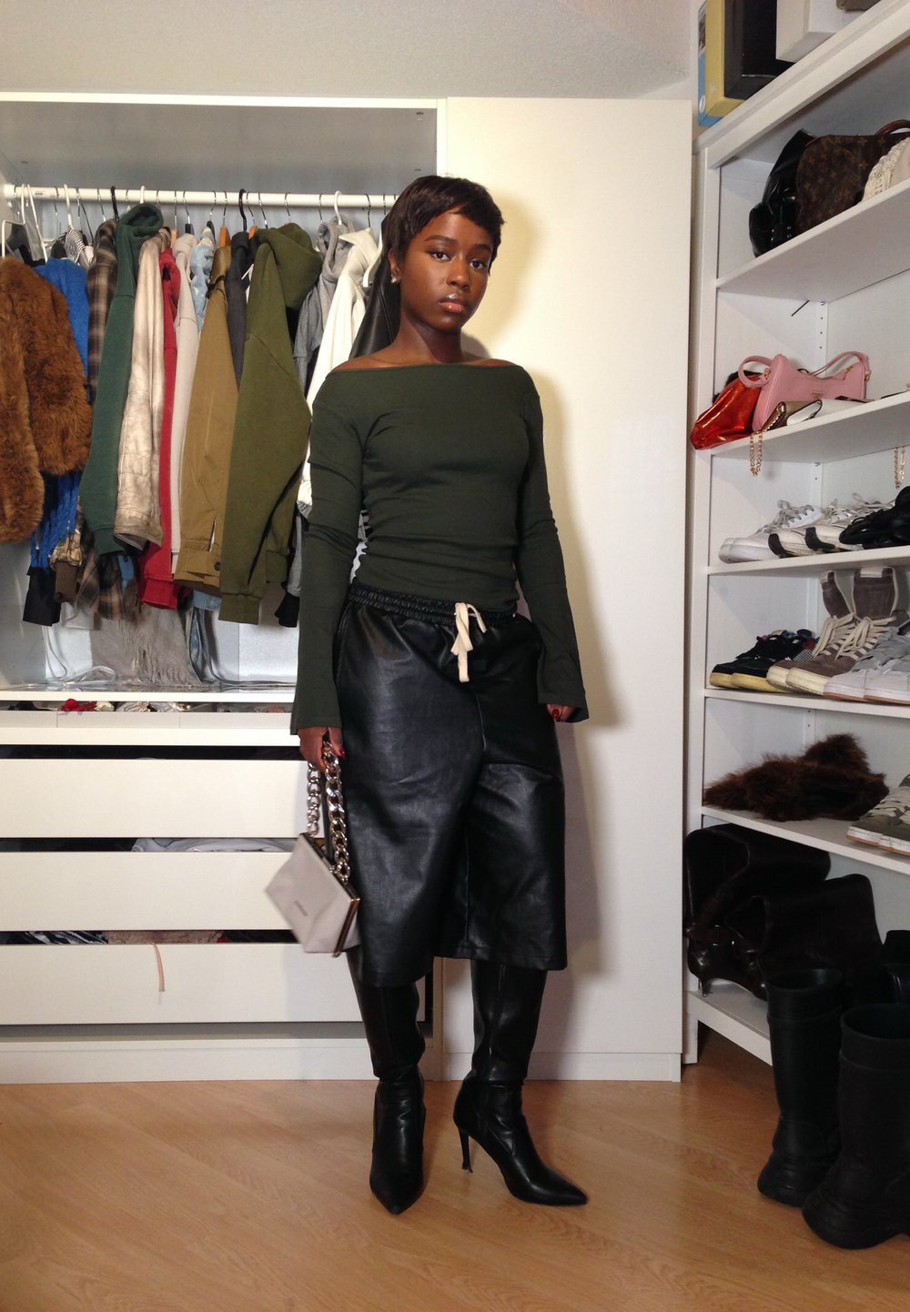 Grøn off-shoulder top, sorte læder culottes med elastisk talje, sorte stiletto støvler, holder en let taske med kædestrop.