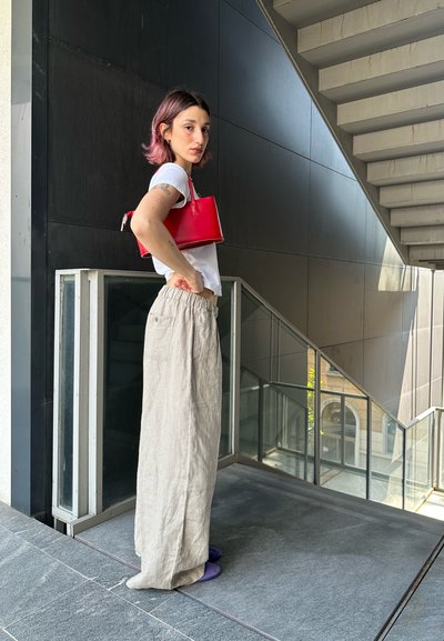 Bolso de mano de cuero rojo con un diseño estructurado, combinado con una camiseta blanca y pantalones de lino beige, con un fondo de escalera moderna.